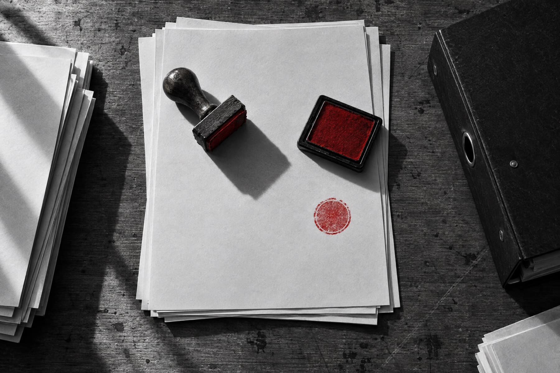 An overhead view of a desk of documents with a rubber stamp and red ink pad.